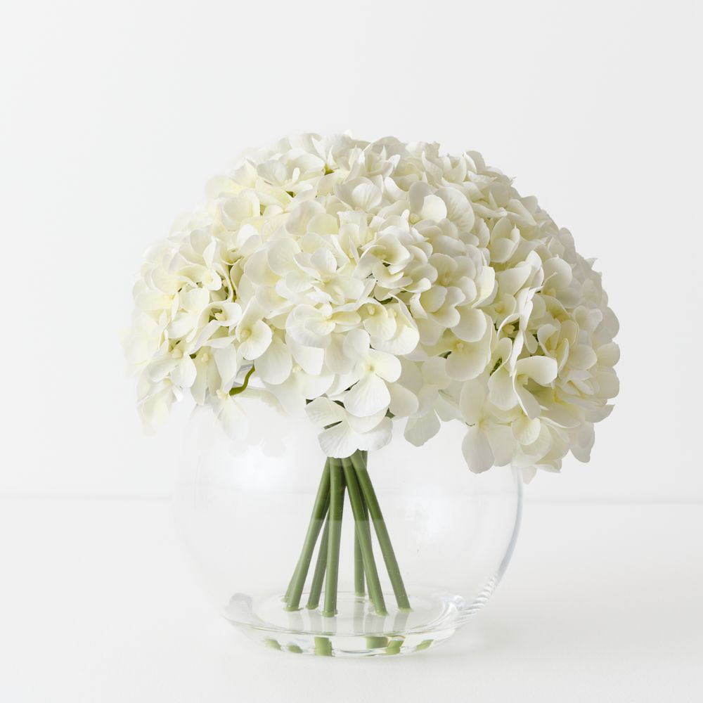 Artificial white hydrangeas in large round glass vase