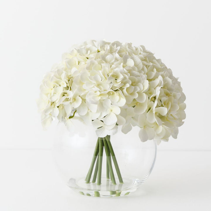 Artificial white hydrangeas in large round glass vase