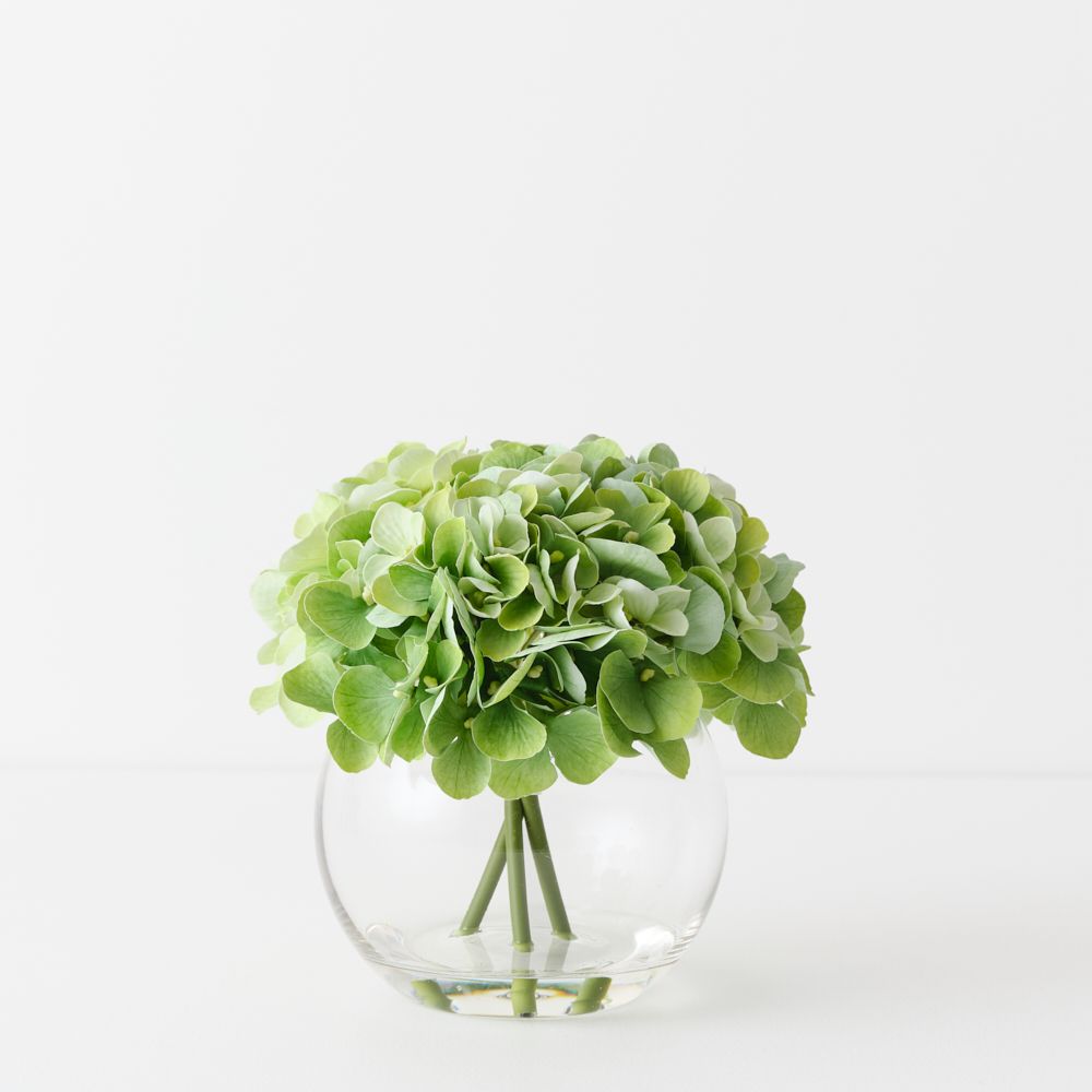 Artificial light green hydrangeas in small round glass vase
