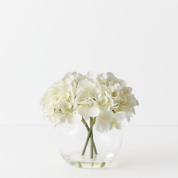 Artificial white hydrangeas in small round glass vase
