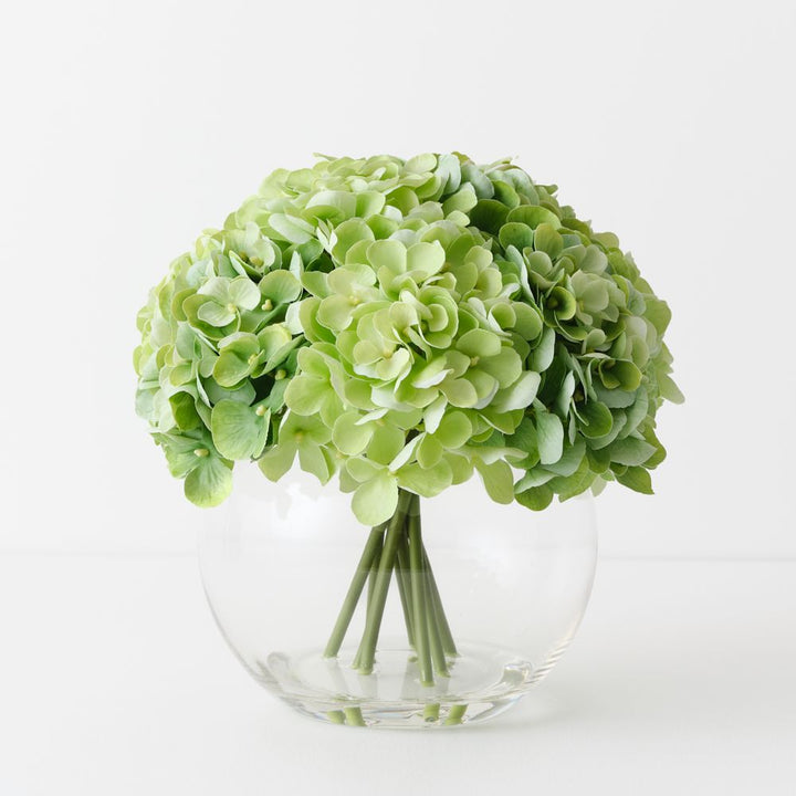 Artificial light green hydrangeas in large round glass vase